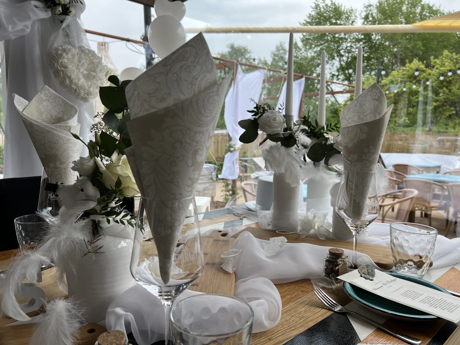 Taparazzi-Restaurant, gedeckter Tisch, auf den Tellern platzierte Menükarten, weiße Serviette im Glas und weiße Rosenblüten